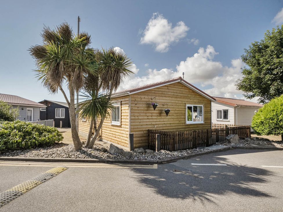 A wooden cabin with palm trees and a gravel area at Seaside Chalet Retreat in Bridlington