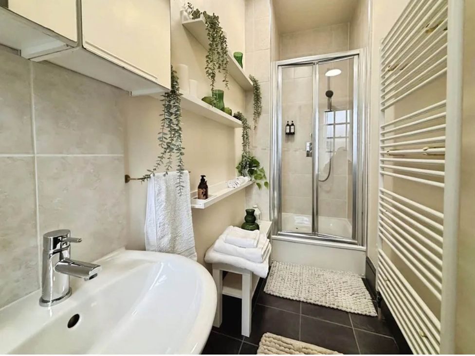A bathroom with a sink, shower, towels, and shelves at 3 Bedrooms in Central Tunbridge Wells