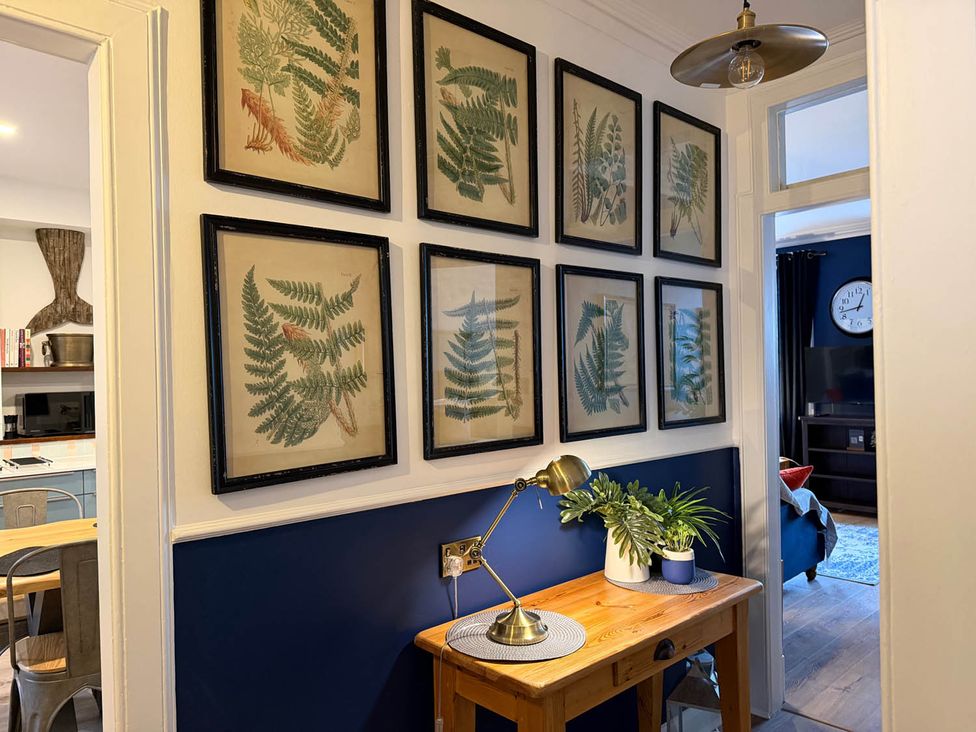 A hallway with framed art on the wall and a wooden table with a lamp and plant at Seaview Apartment 2Bed on Anstruther Harbour in Anstruther
