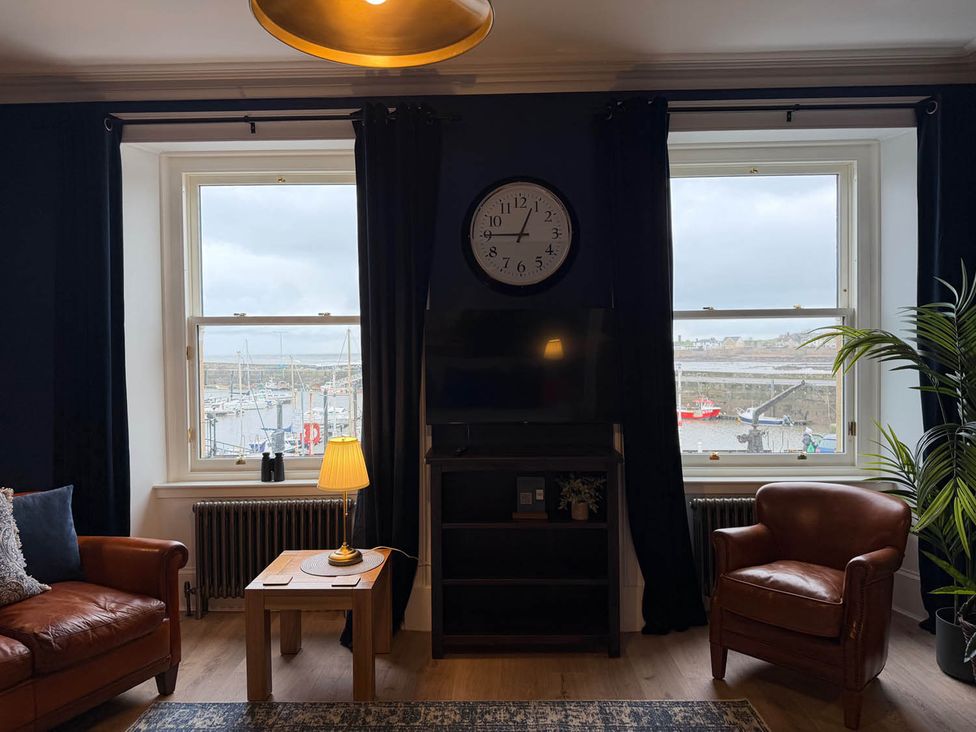 A living room with a television, clock, and windows at Seaview Apartment 2Bed on Anstruther Harbour Anstruther