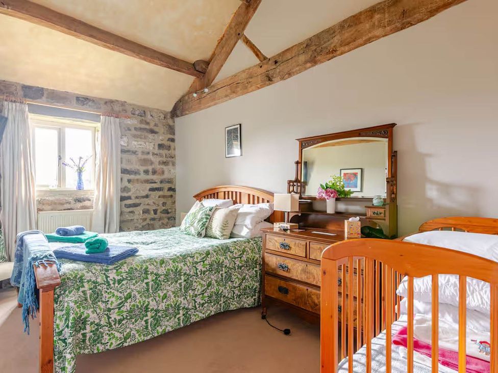 A bedroom with a double bed and a baby crib at Dowgill 3Bed Barn Sleeps 7 Hot Tub Parking Near Summerbridge