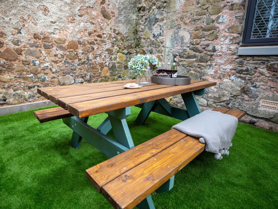 A picnic table with flowers and a wine bottle in an outdoor seating area at Stunning 3 Bed Converted Village Hall Near Kelso Nenthorn near Kelso