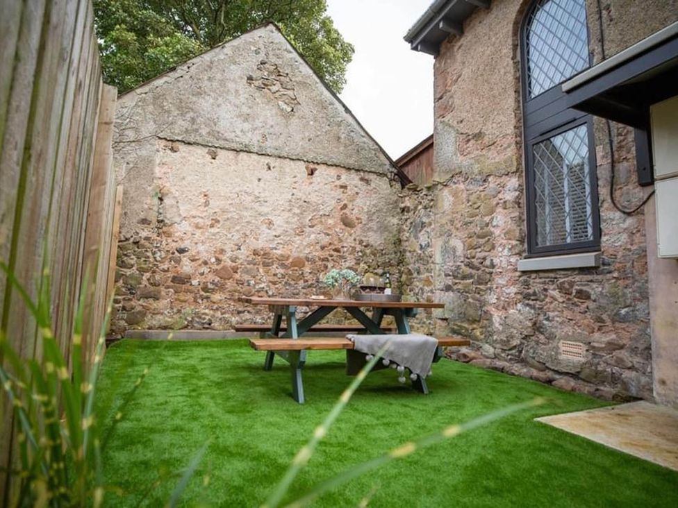 A garden with a stone wall and a picnic table at Stunning 3 Bed Converted Village Hall Near Kelso