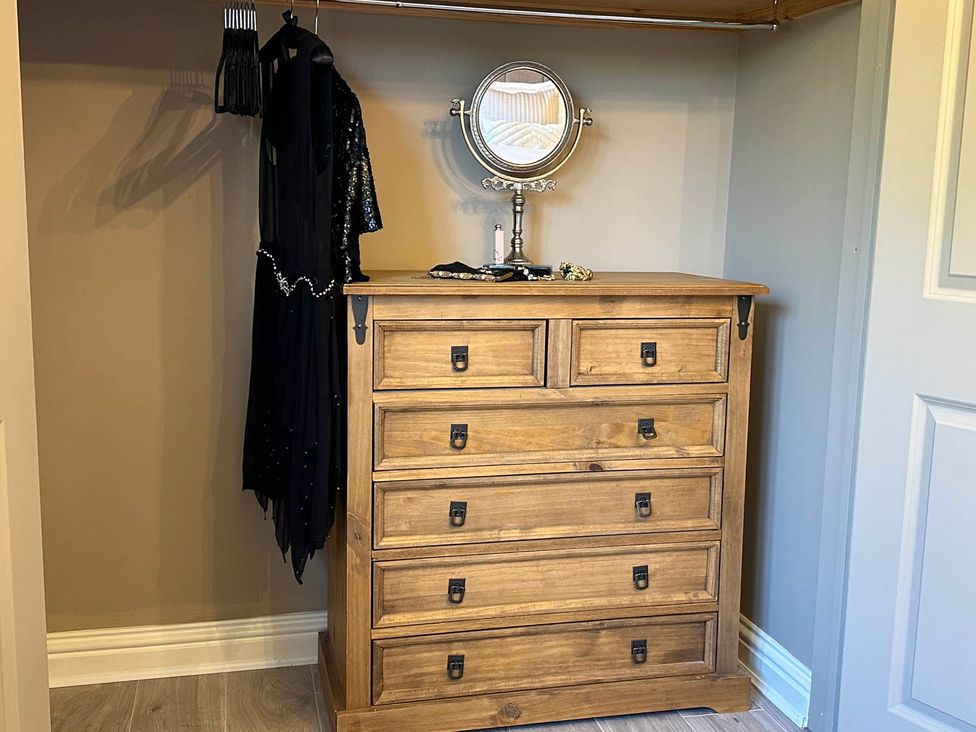 A bedroom with a dresser and dress hanging in the closet at Cottage Sleep 4 Pet Friendly Enclosed Garden, Rollesby, near Scratby