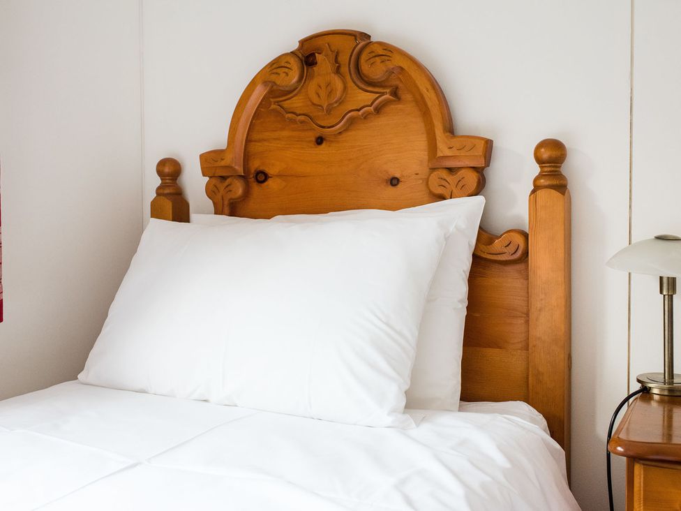 A bed with a wooden headboard and white pillows at a 2 bedroom lodge with free WiFi and mountain view near Crianlarich