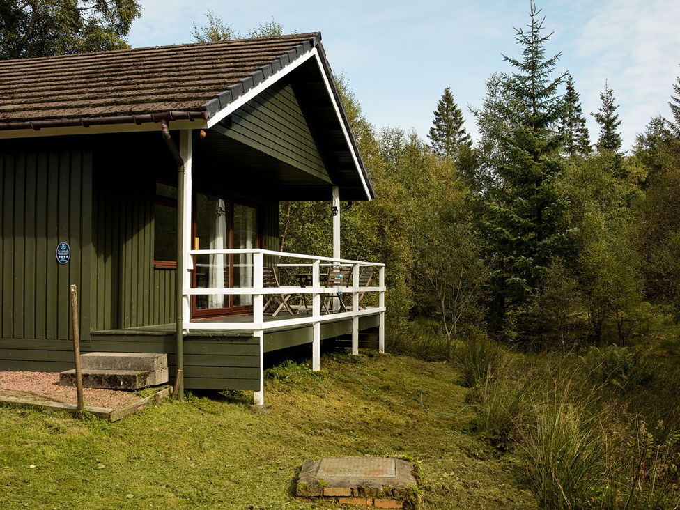 A lodge with a deck and outdoor seating near trees at 2 bedroom lodge with free WiFi and mountain view near Crianlarich