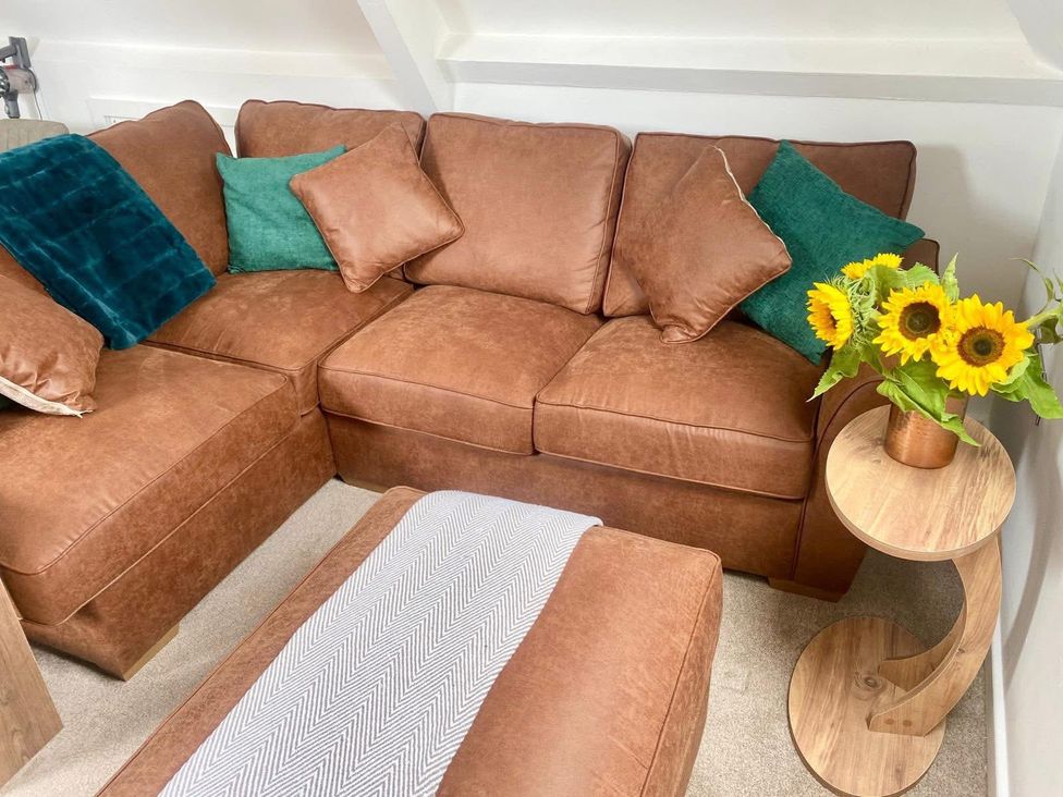 A living room with a brown sofa and a table with flowers at Central Tenby 3 Bed Apt Sleeps 6 to 8 Dog Friendly in Tenby