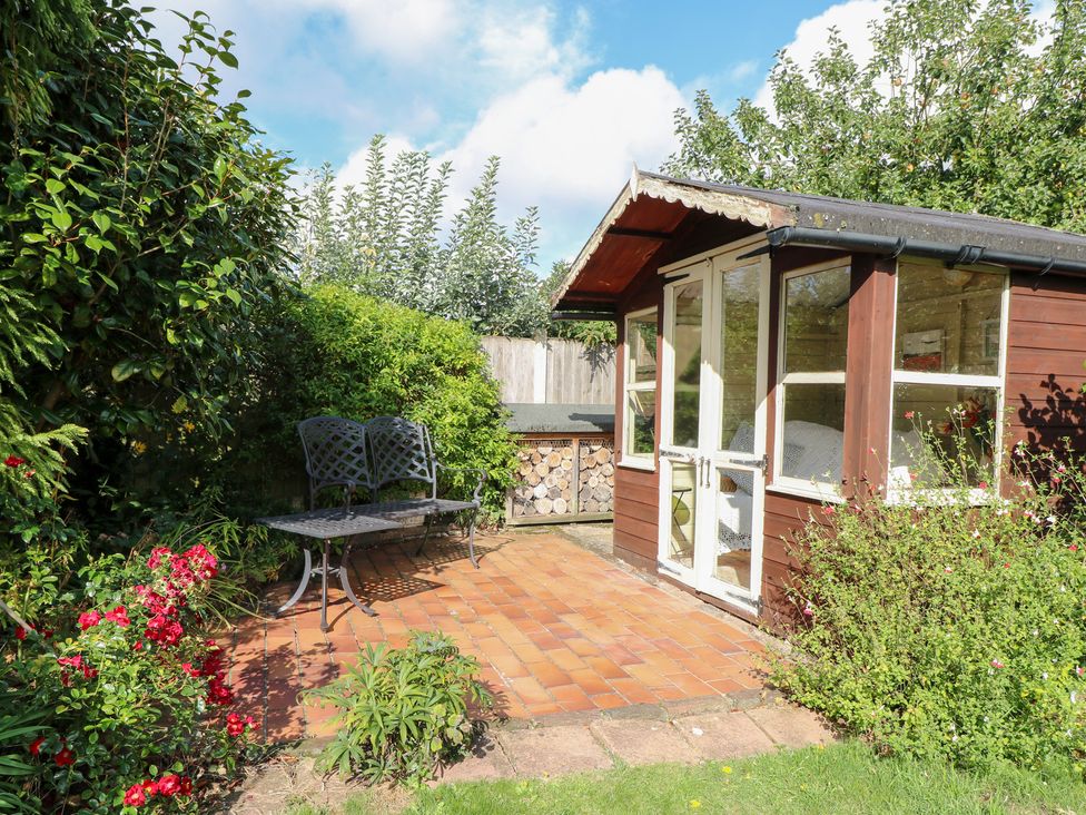 A garden shed with a paved patio and a bench at Hollyhedge Cottage in Briston