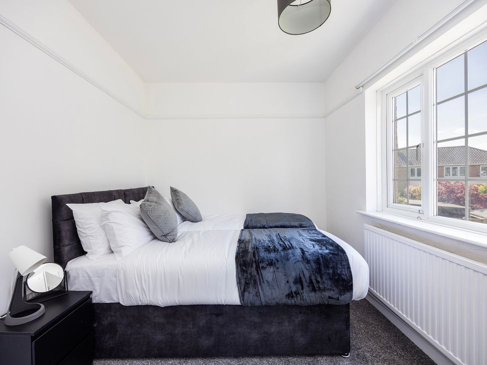 A bedroom with a bed, bedside table, lamp and window at House Sleeps 14 with Parking and Garden East Tilbury