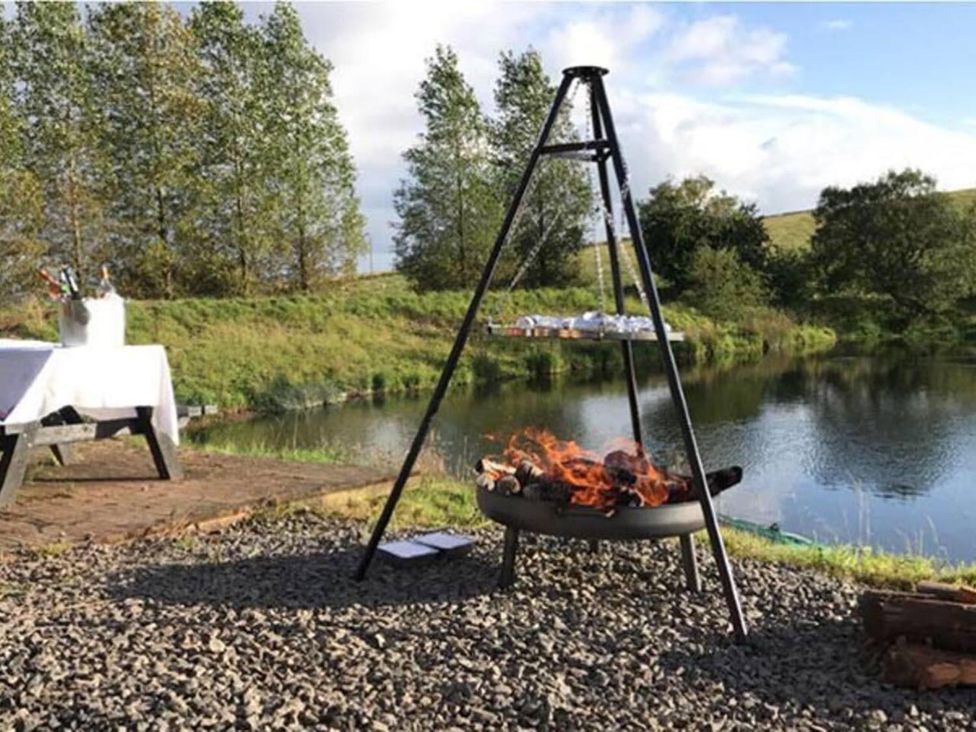 An outdoor area with a fire pit and a table near water at Luxury Duplex Sleeps 2 Hot Tub Balcony Parking Duncrievie near Milnathort