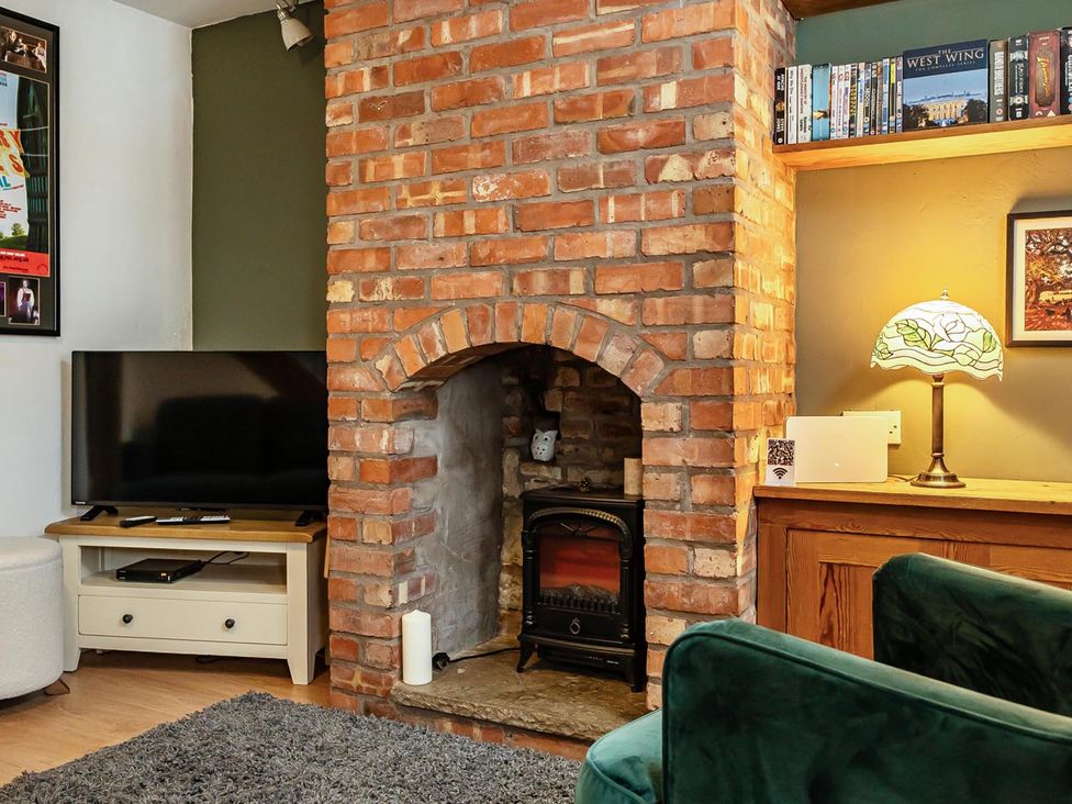 A living room with a brick fireplace and television at Quaint Cottage in Charming Evesham