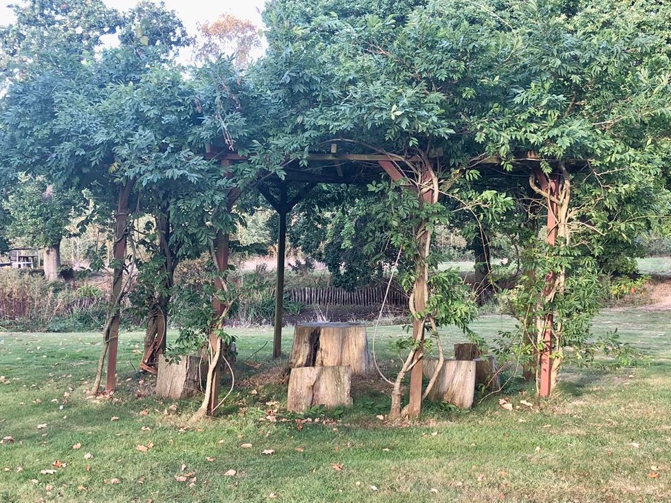 A pergola with wooden benches and stumps in a garden at Tyler Hill near Canterbury