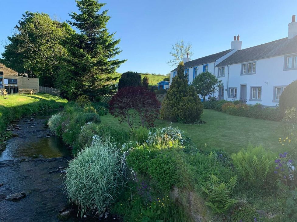 A garden with a stream and house at House Sleeps 10 Pet friendly Parking in Caldbeck
