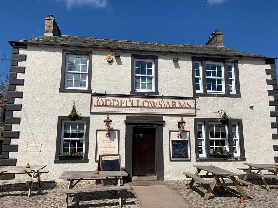 A pub exterior with tables and signage at Oddfellows Arms in Caldbeck