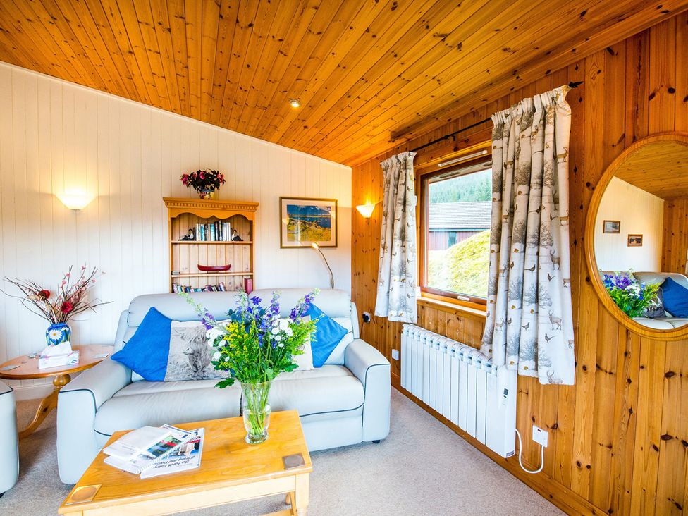A living room with a sofa and bookshelves at Raven Lodge with beautiful views of Loch Dochart Near Crianlarich