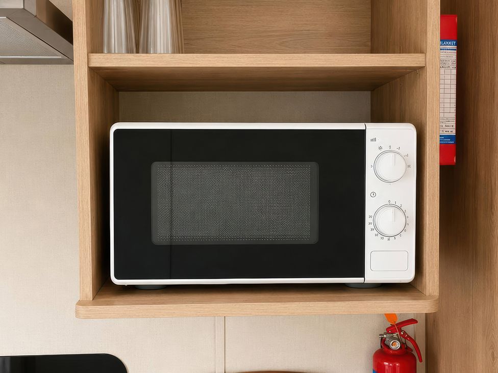 A microwave on a shelf with glasses and a fire extinguisher in a kitchen