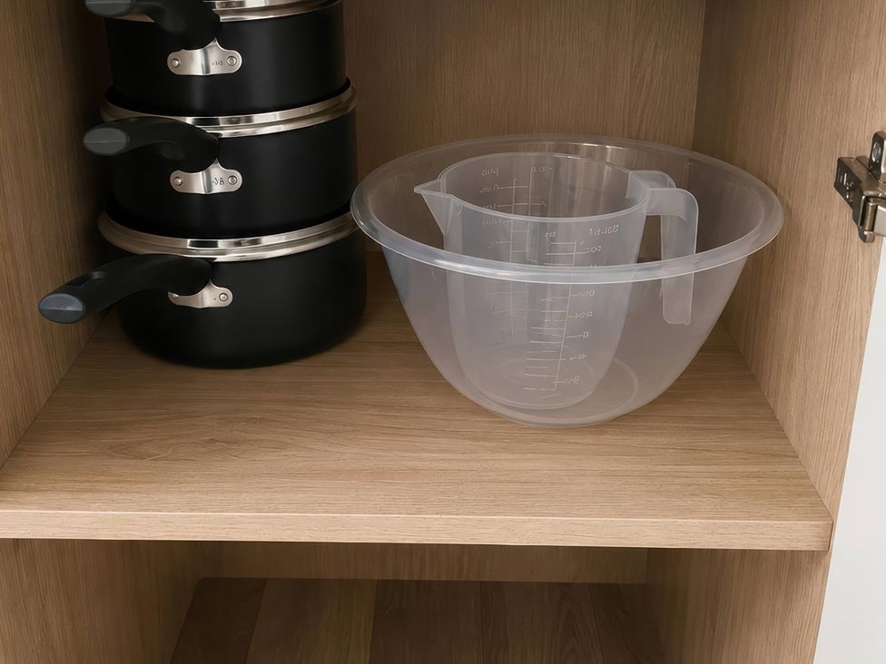 A kitchen cabinet with stacked pans and a measuring bowl