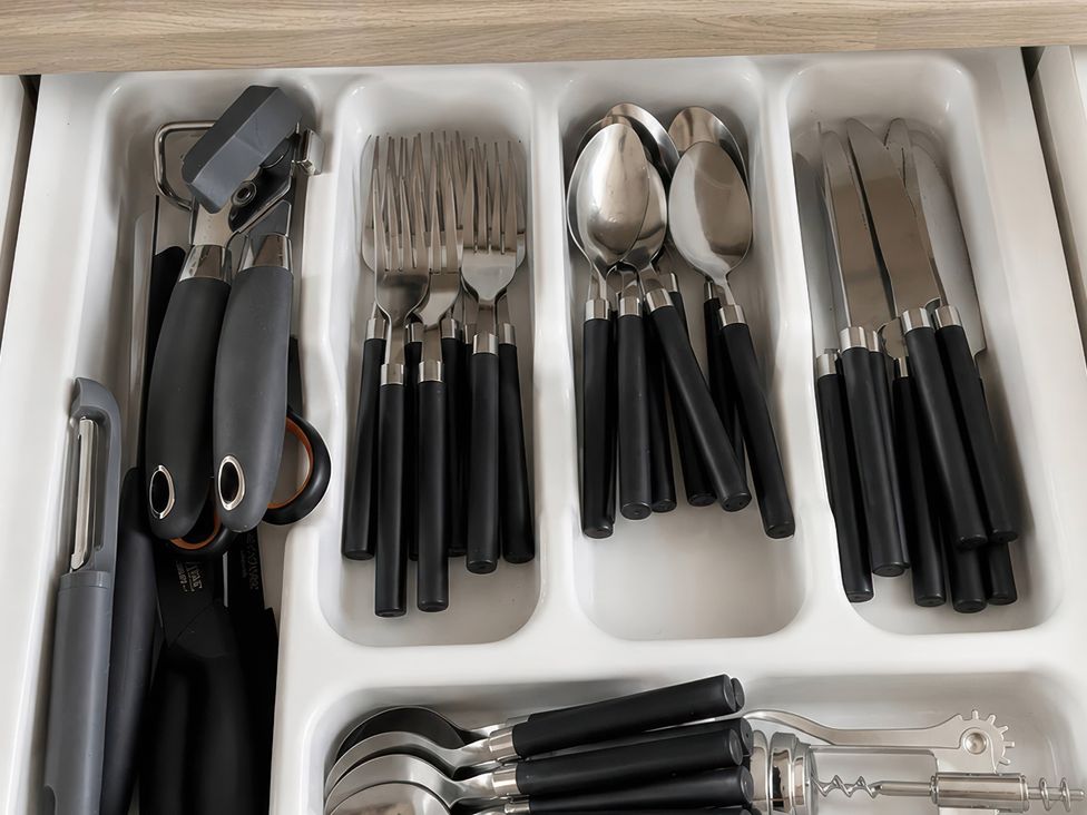 A drawer containing forks, spoons, knives, and kitchen utensils in a kitchen