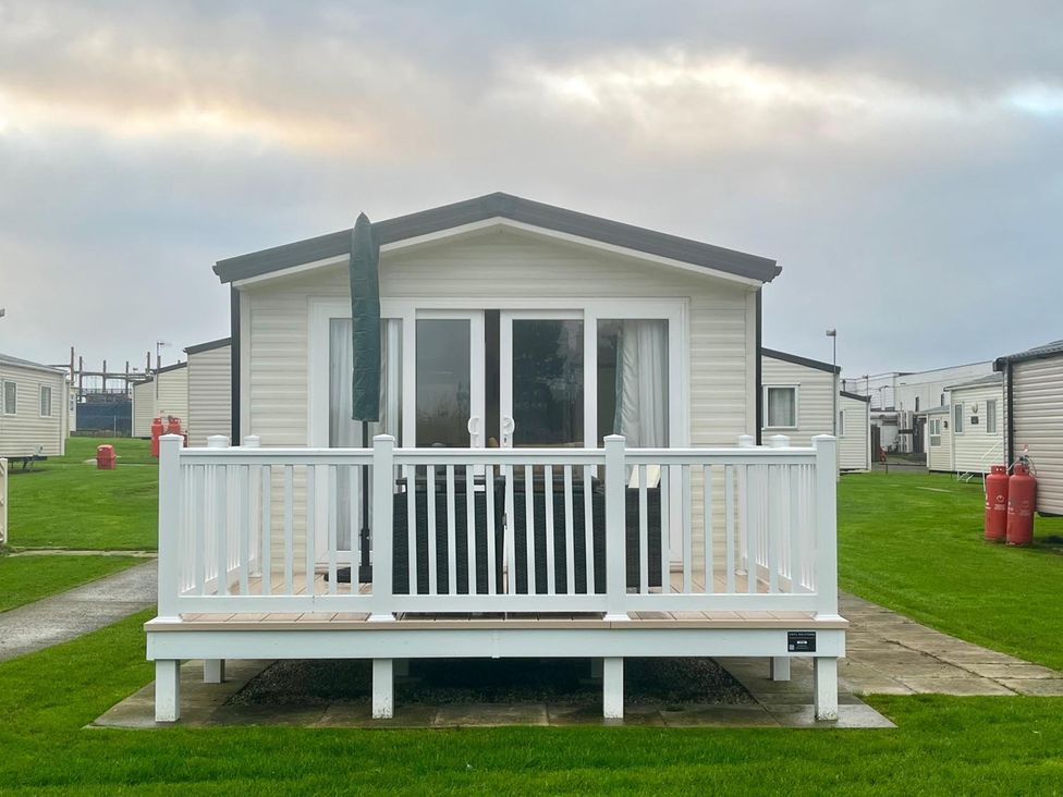 A caravan with a deck in a grassy area at Surfside Bliss Cayton Bay Park caravan, Cayton Bay