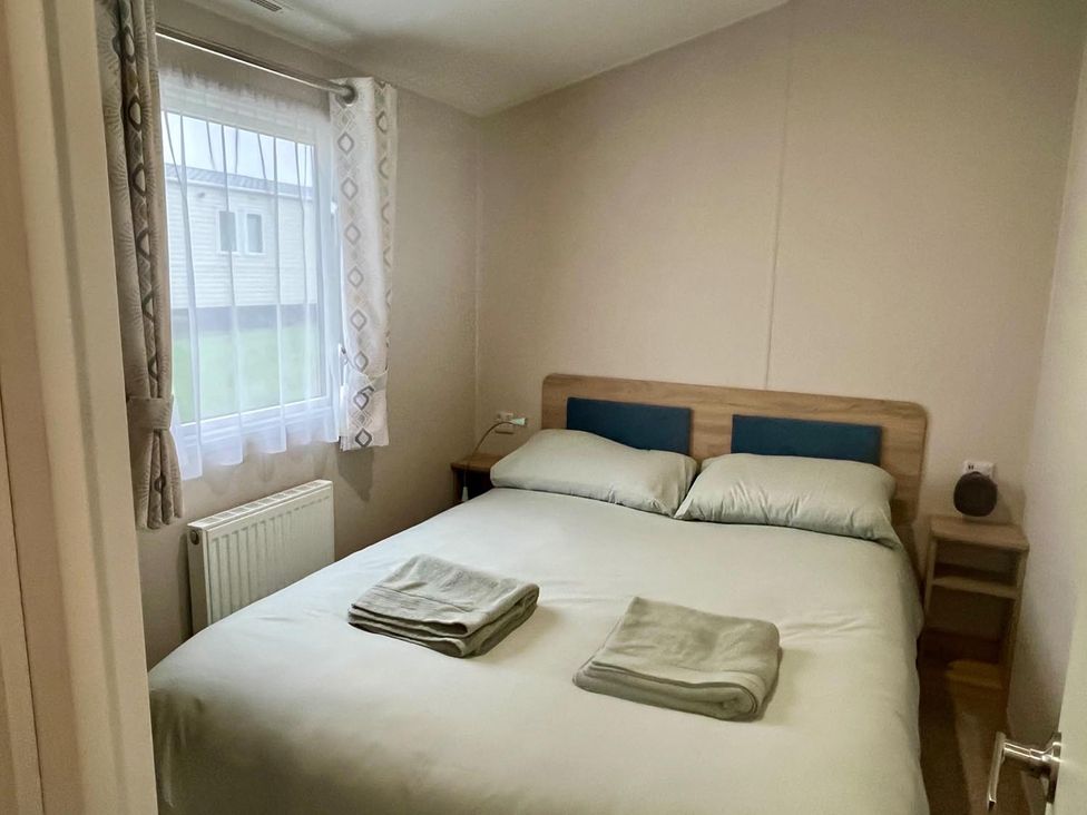 A bedroom with a double bed and nightstand at Surfside Bliss Cayton Bay Park caravan in Cayton Bay