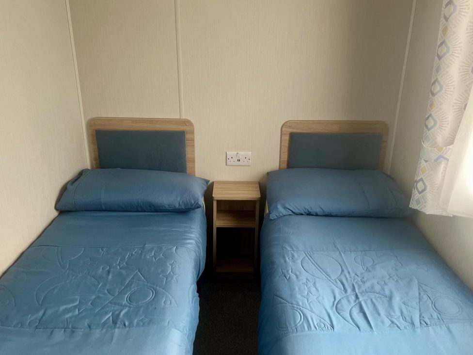 A bedroom with two beds and a nightstand at Surfside Bliss Cayton Bay Park caravan in Cayton Bay