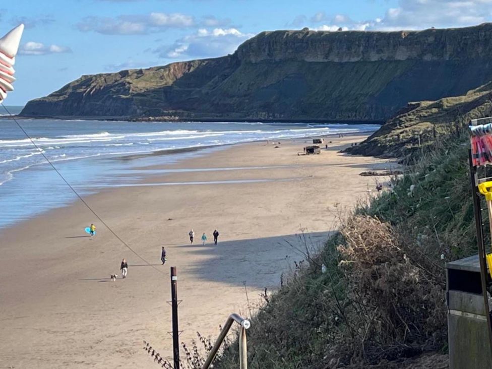 A beach with cliffs and people walking at Surfside Bliss Cayton Bay Park caravan in Cayton Bay