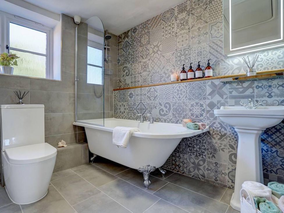 A bathroom with a bathtub, toilet, sink, and decorative items at 1 Bed Cottage Sleeps 2 with Hot Tub Pets Welcome, Great Massingham