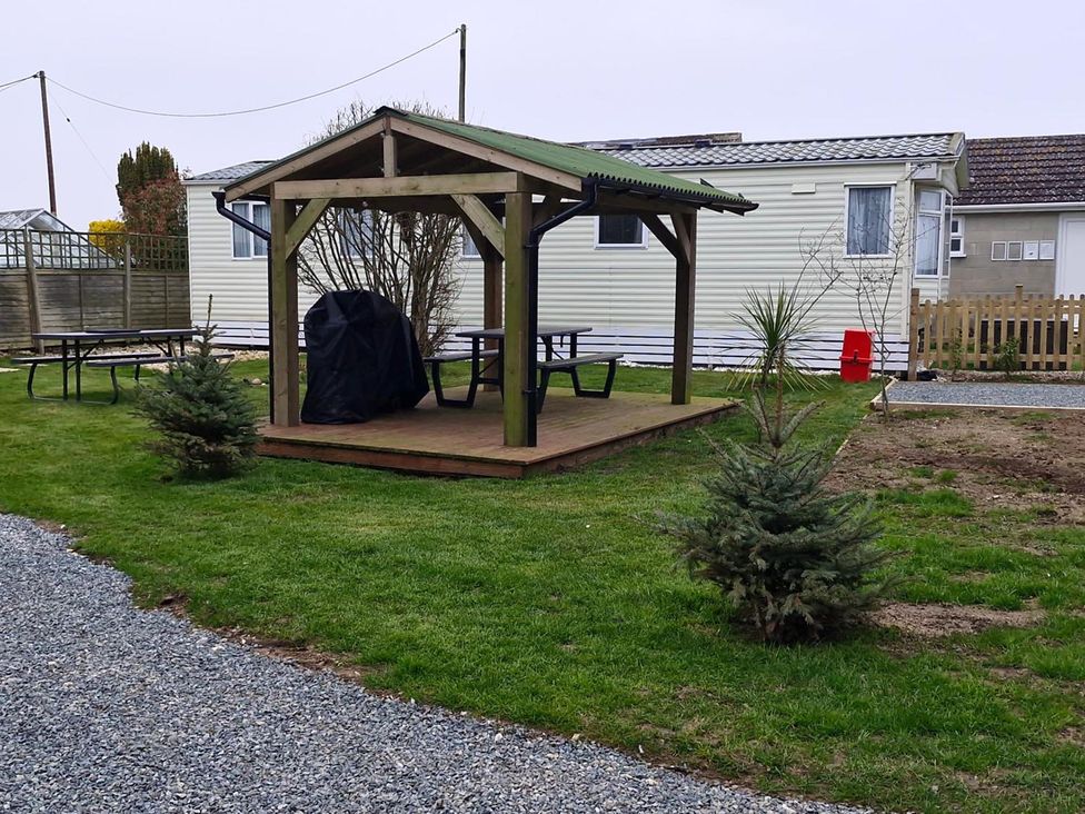 A gazebo with a grill and tables in a garden at Woodland View Dog Friendly Nr Sutton on Sea Thurlby near Alford