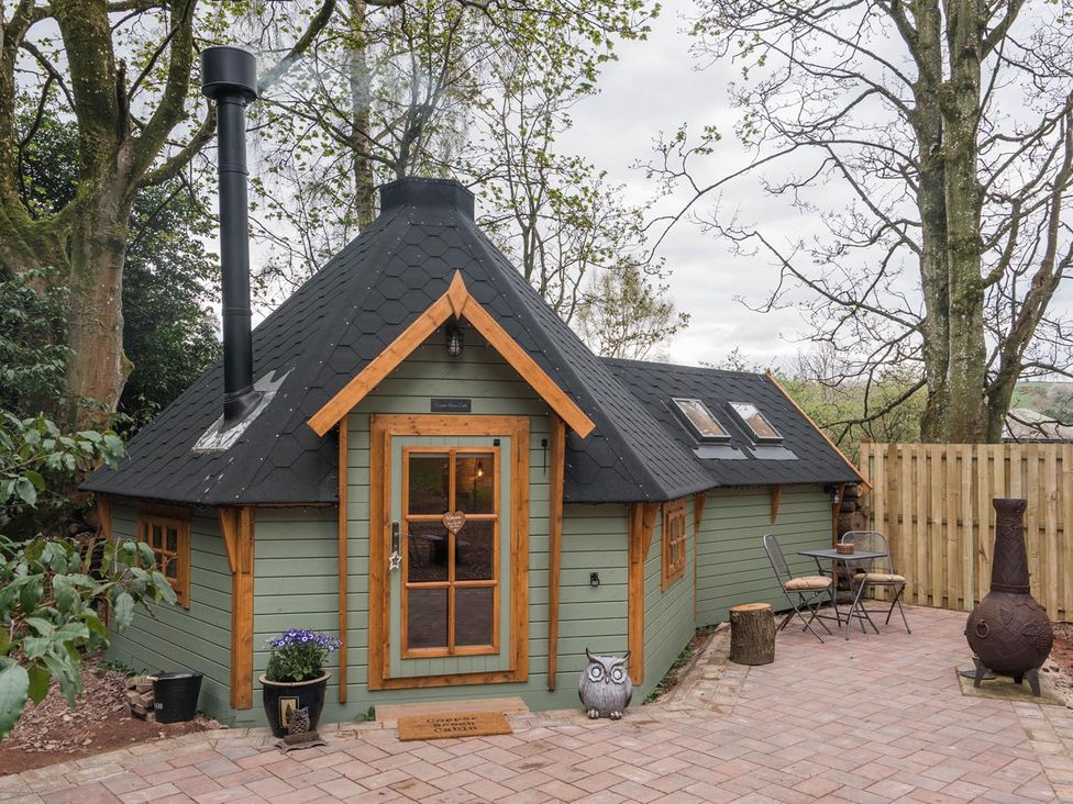 A cabin with a chimney and patio area at Punch Tree Cabins Outdoor Bath Wood Burner in Carluke near Larkhall