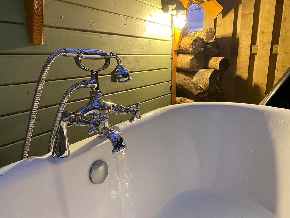 A bathtub with a faucet and water running at Punch Tree Cabins Outdoor Bath Wood Burner in Carluke near Larkhall
