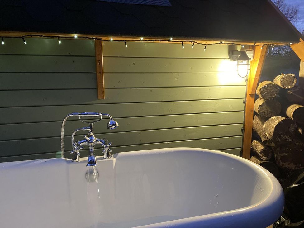 A bathtub with a faucet in an outdoor bath area at Punch Tree Cabins Outdoor Bath Wood Burner in Carluke near Larkhall