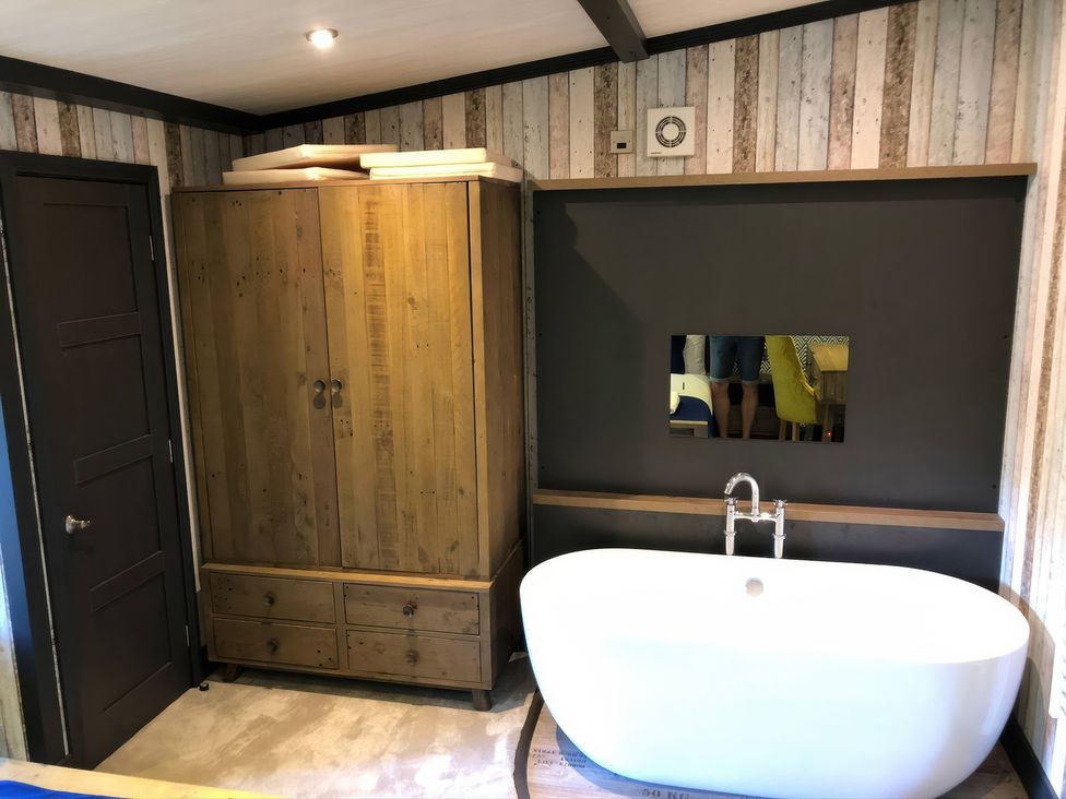 A bathroom with a bathtub and a wooden cabinet at Sandy Balls Holiday Park Pet Friendly Lodge in Godshill, Hampshire
