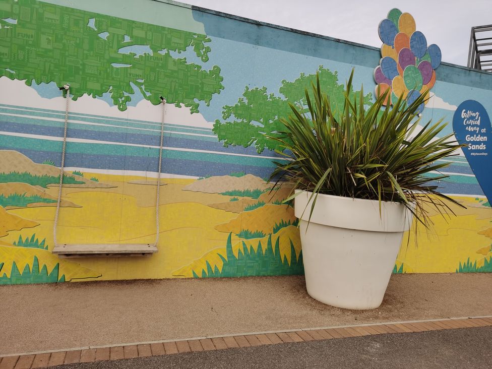 An outdoor area with a swing, wall mural and large planter at Golden Sands