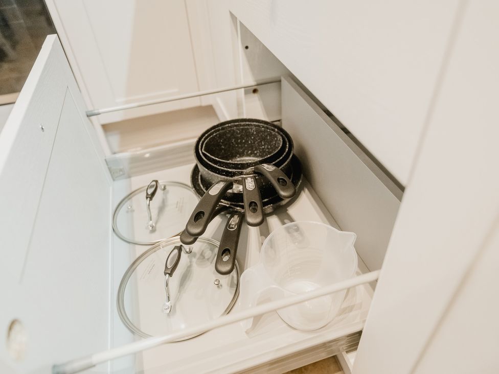 A kitchen drawer with pans, lids and a measuring cup at 