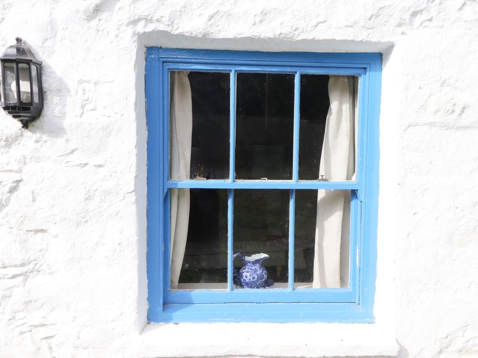 A window with blue frame and curtains at Felin Bach in Aberdaron