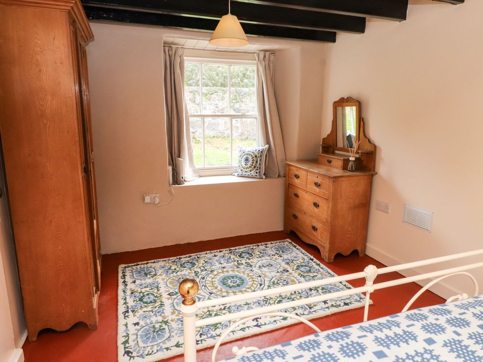 A bedroom with a wardrobe, window, rug, and dresser at Felin Bach in Aberdaron