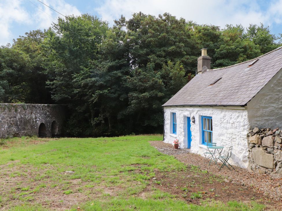 A cottage with a table and chair near a stone bridge at Felin Bach Aberdaron