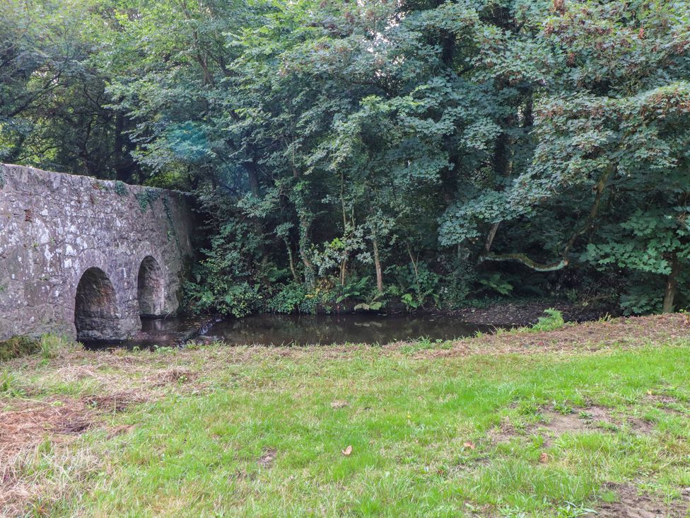 A stone bridge over a stream surrounded by grass and trees at Felin Bach Aberdaron