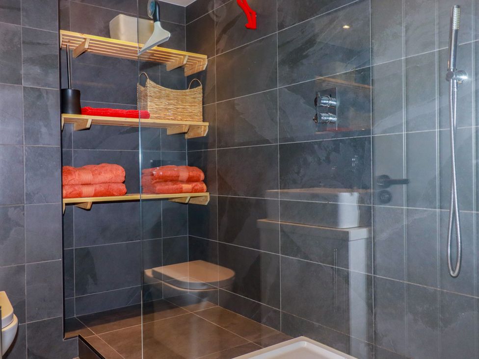 A bathroom with a shower, toilet, and towels arranged on shelves at Mermaid Gaze in Newquay
