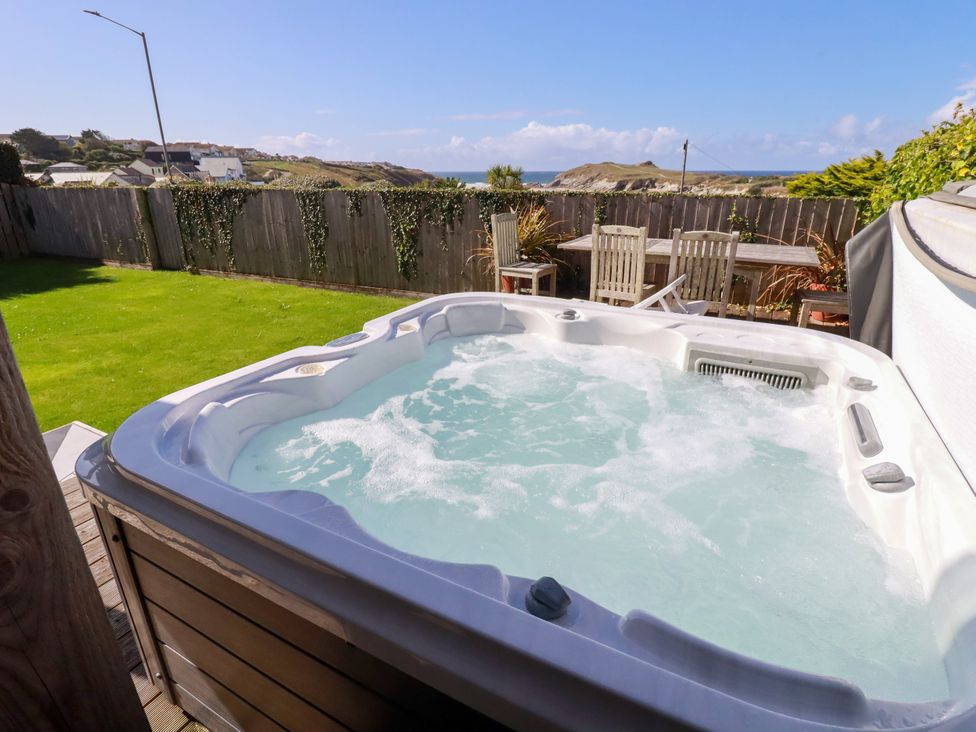 A hot tub surrounded by a garden with seating at Mermaid Gaze in Newquay