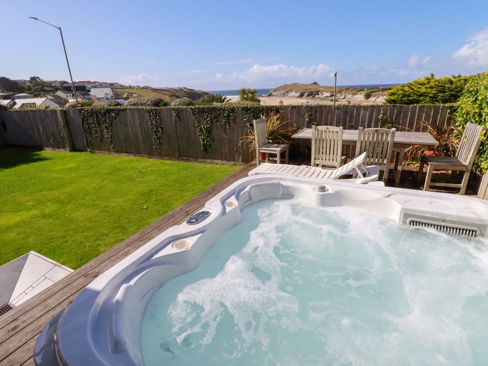 A hot tub on a wooden deck with a garden table and chairs at Mermaid Gaze in Newquay