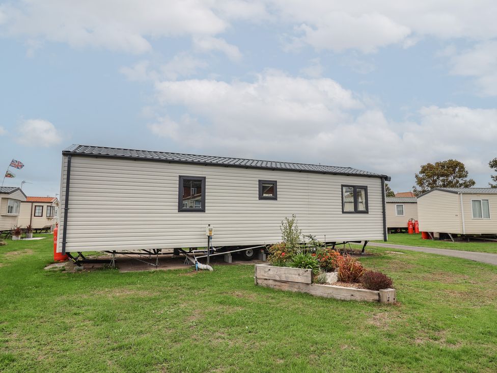 A mobile home positioned on grass with a flower bed at S7 Abergele
