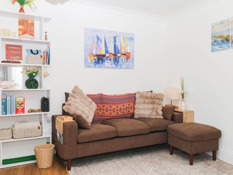 A living room with a sofa, cushions, shelf with books, and lamp at Elberry Cove View in Paignton