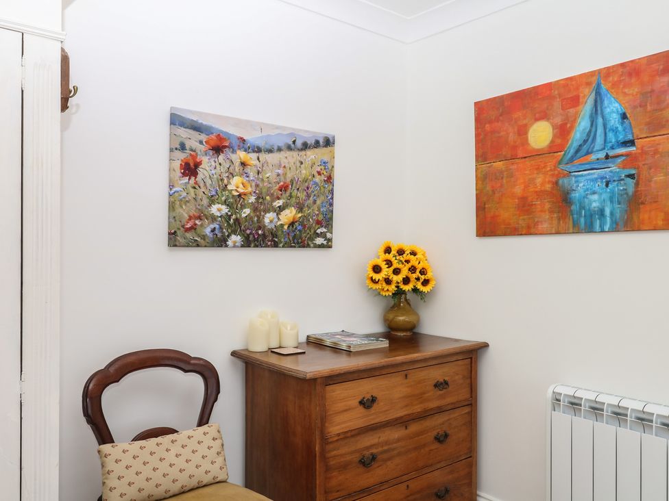 A hallway with a dresser, sunflowers in a vase and two paintings at Elberry Cove View Paignton