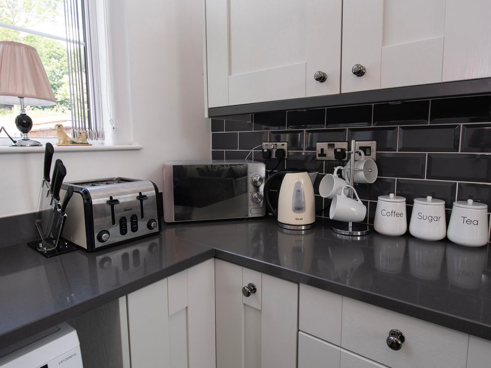 A kitchen countertop with a toaster, microwave, kettle, mugs, and canisters at The Old School House