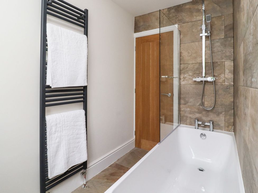 A bathroom with a bathtub and towel rack at Cottage by the River Burnley