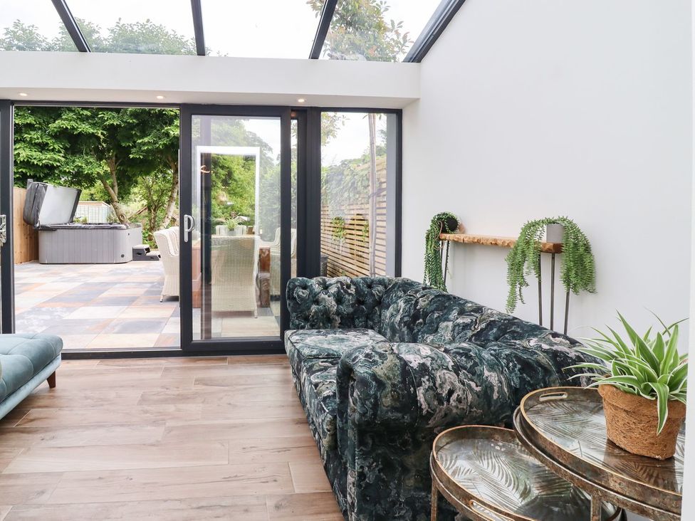 A conservatory with a sofa and glass doors leading to outdoor space at Cottage by the River in Burnley