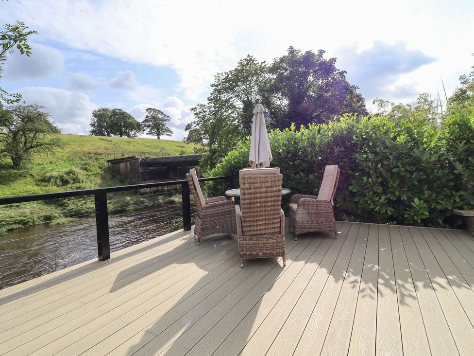 An outdoor seating area with a table and chairs near a river at Cottage by the River Burnley