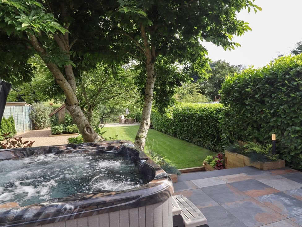 A garden with a hot tub, trees, and grass at Cottage by the River Burnley