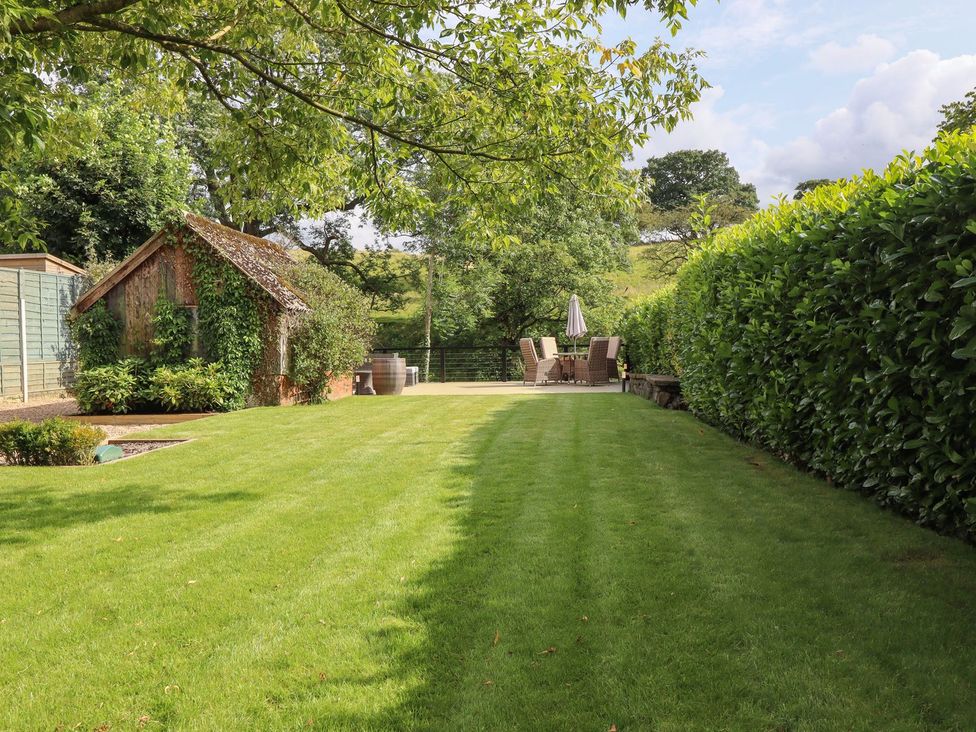A garden with grass, patio furniture, and a wooden shed at Cottage by the River Burnley